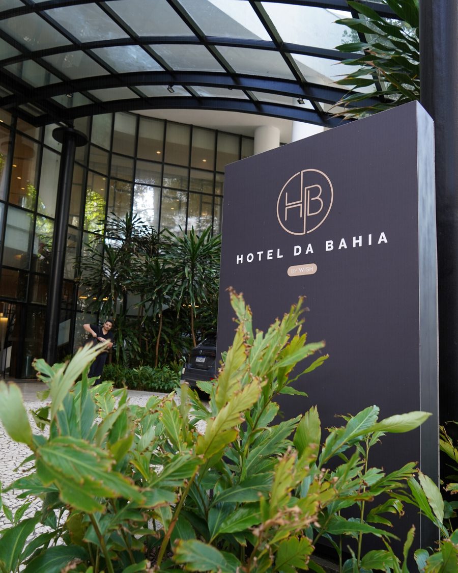 Entrada do Hotel da Bahia by Wish, com a placa do hotel em frente à fachada de vidro